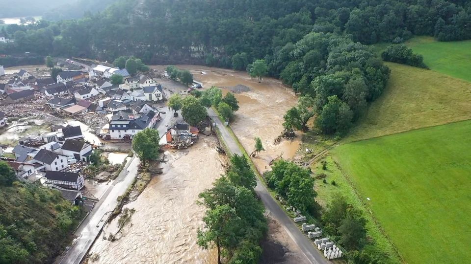 Auf einer Luftaufnahme ist ein Ort zu sehen, um den sich ein Hochwasser führender brauner Fluss windet